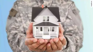 A military personnel holds a house mockup with both hands. Applying for a VA loan.